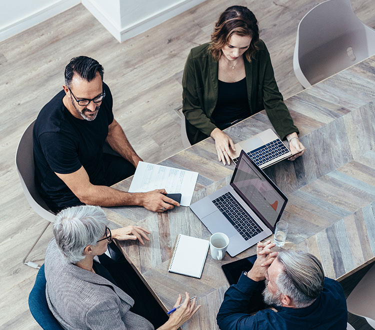 A group of professionals is engaged in a business meeting around a table with laptops, documents, and a coffee cup.