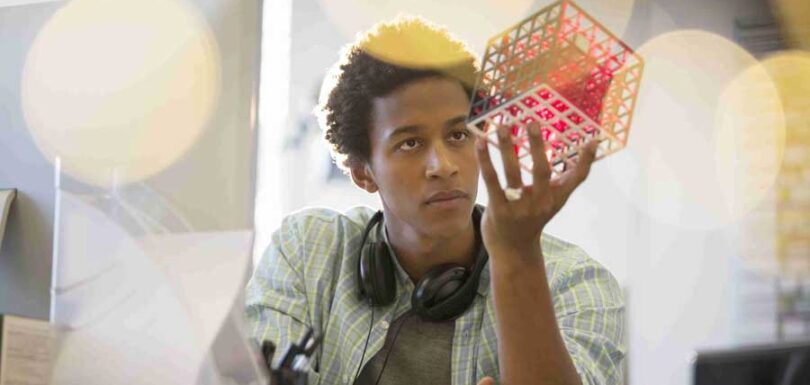 a man is holding a red cube in front of his computer